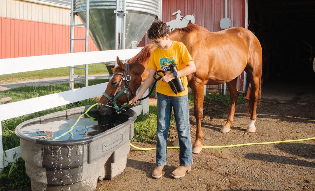 a boy holding binoculars and drinking water from a trough