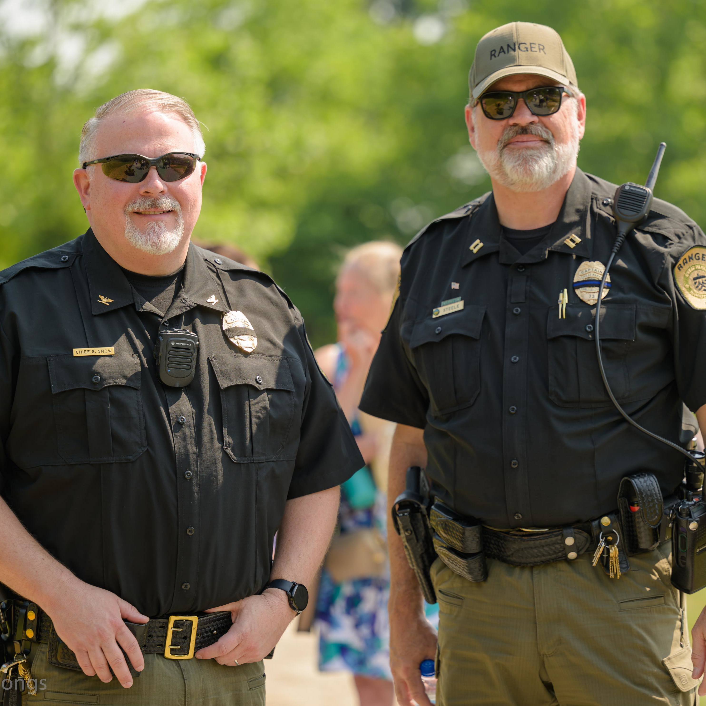 two rangers in their law enforcement uniforms standing in front of blurred trees