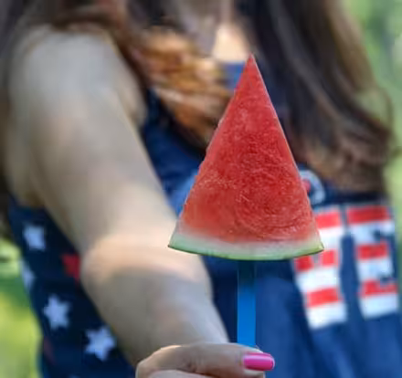 a hand holding a watermelon on a stick